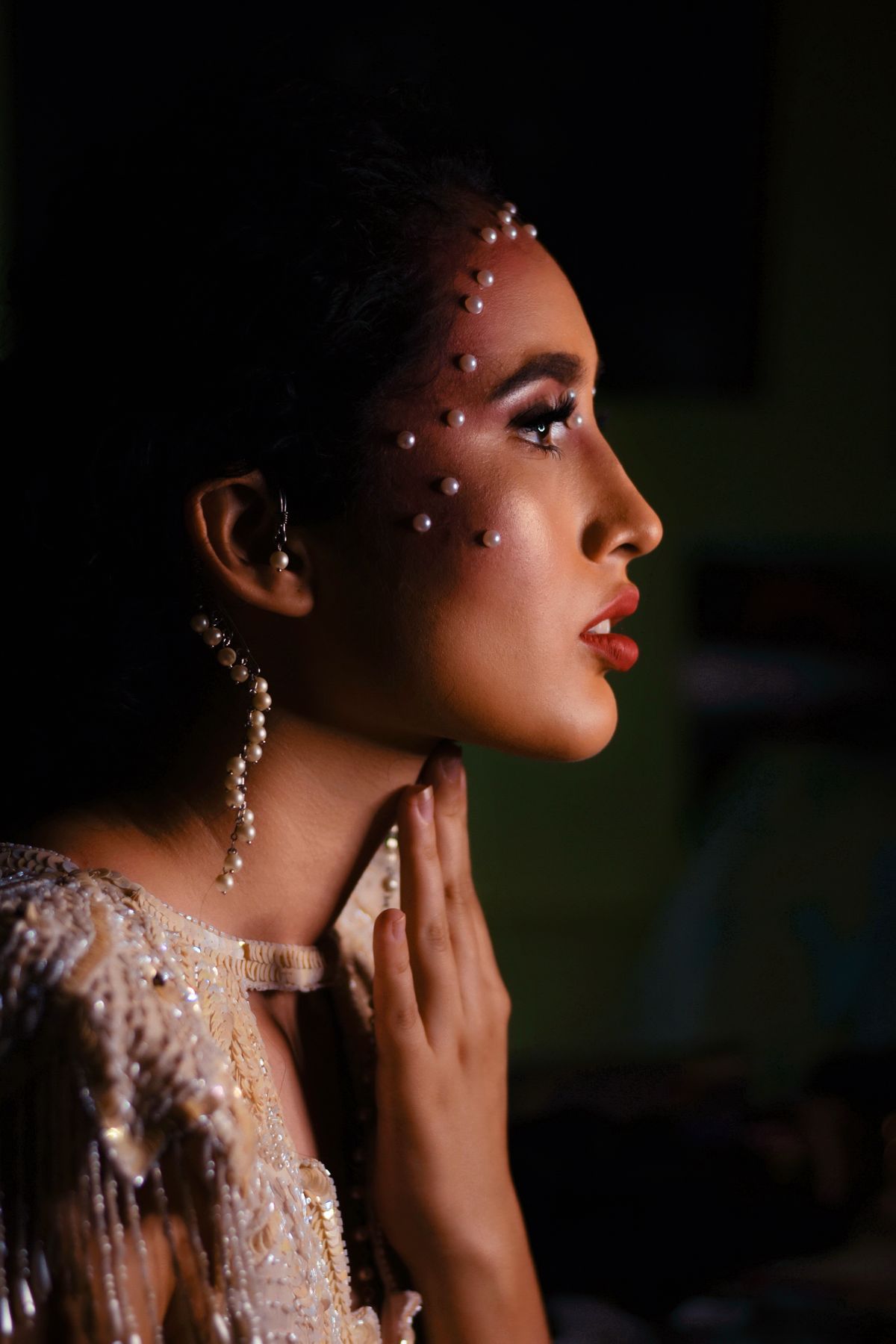 Profile portrait of a woman adorned with pearls and elegant jewelry, set against a dark backdrop.