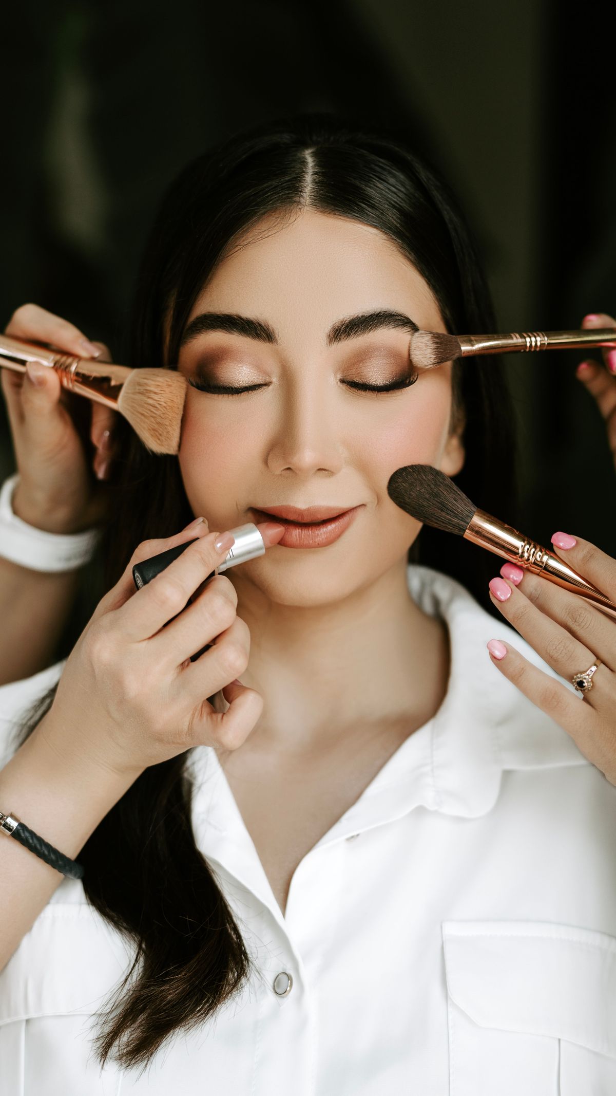 Close-up of a bride receiving a professional makeup look with various brushes and tools.