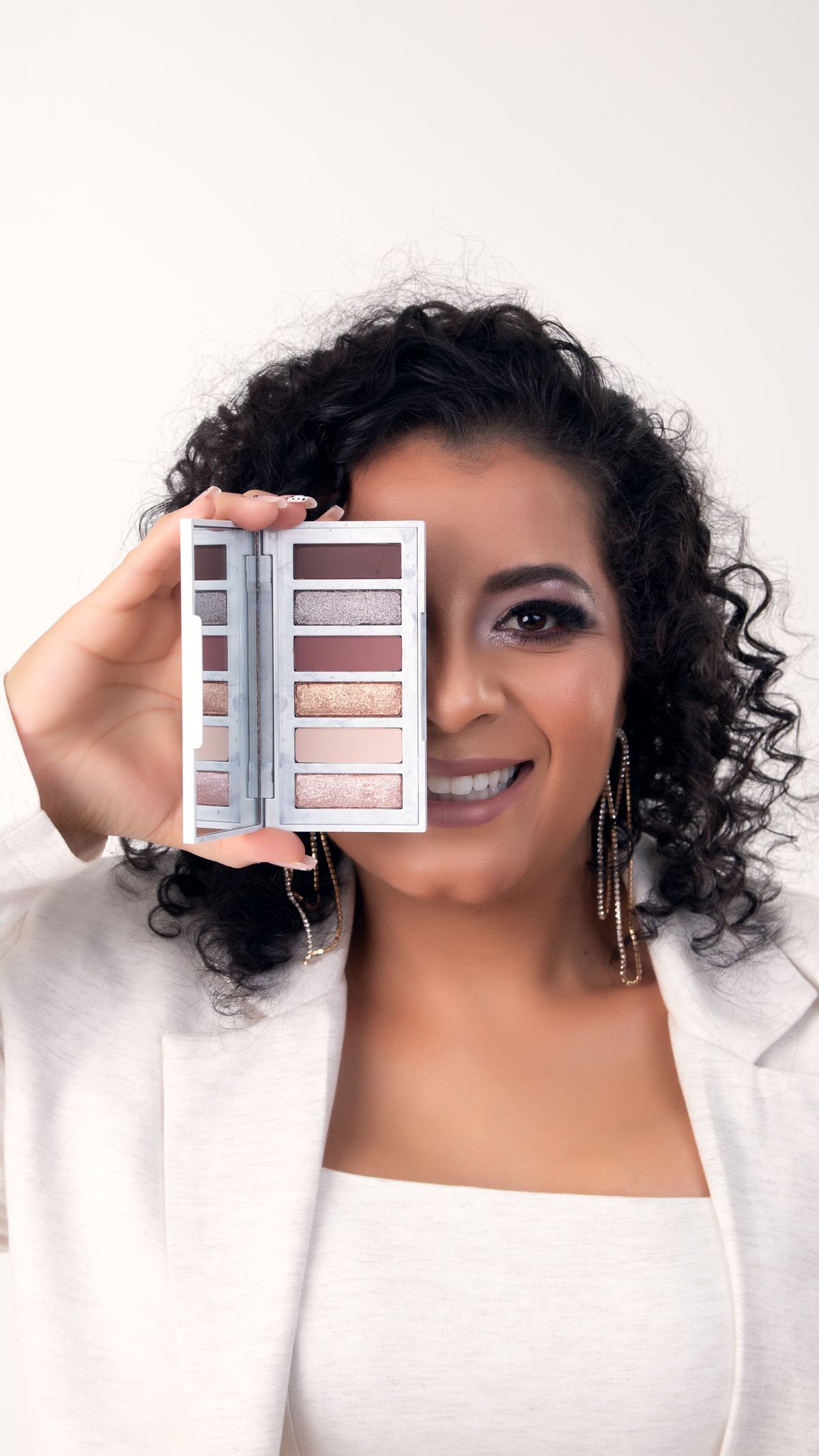 Woman showcasing an eyeshadow palette with a smile, perfect for beauty and makeup themes.