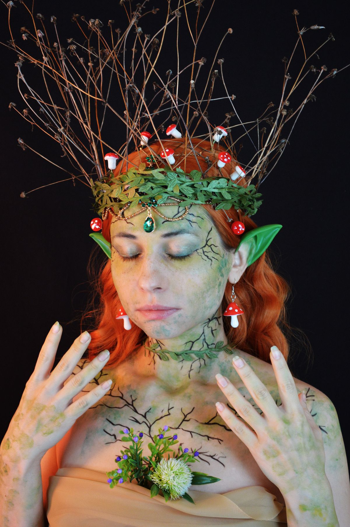 Serious young lady wearing enchantress costume with green wreath with twigs and decorative small mushrooms in hair and fake ears with body art with closed eyes on black background