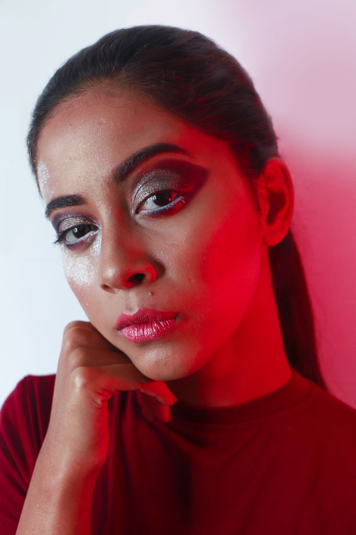 Close-up portrait of a woman with bold makeup and red lighting creating a striking effect.