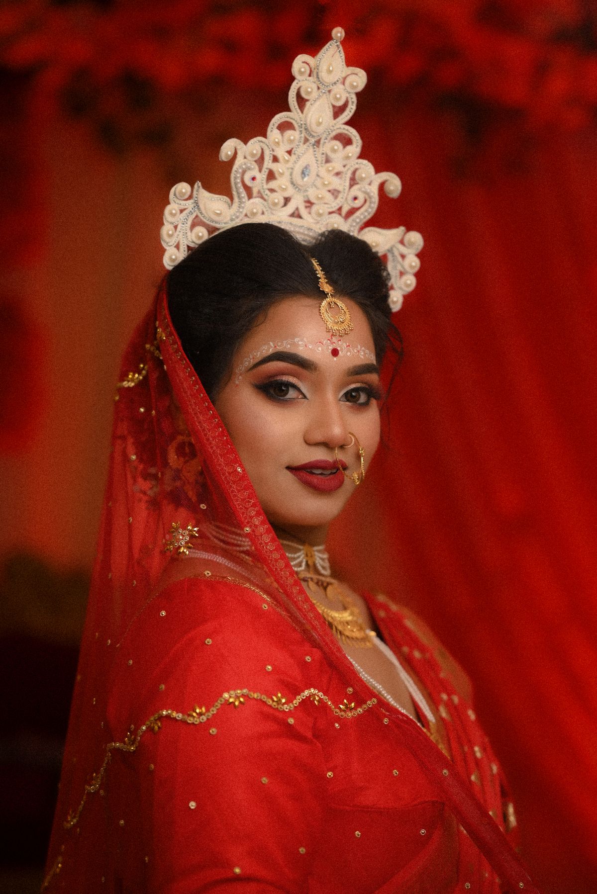 A beautiful bride in traditional red attire with intricate jewelry and a decorative crown.